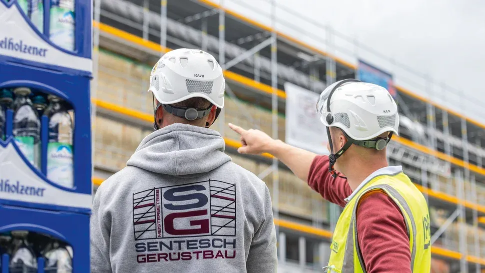 Zwei Sentesch-Monteure mit Helm besprechen sich am Gerüst